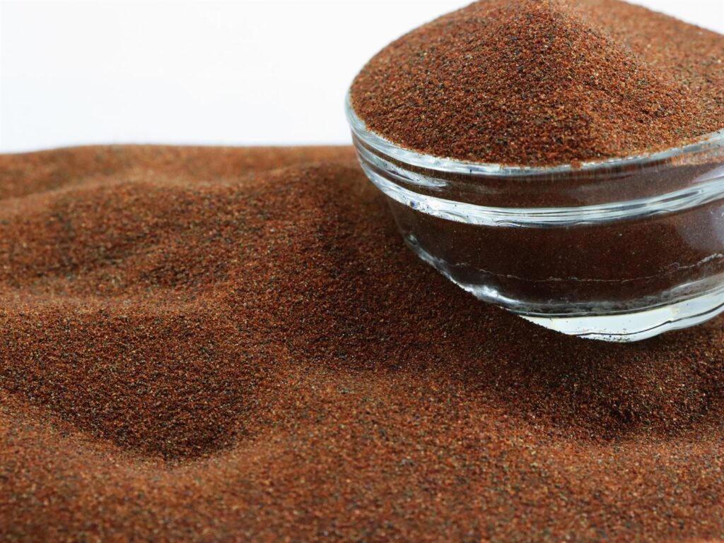 Waterjet garnet abrasive 80A+ 80 mesh — reddish brown angular rock garnet grains in a glass bowl